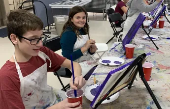 boy painting at table easle